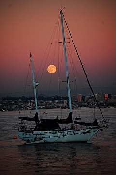 Full moon rises between the masts of a wooden schooner in San Diego